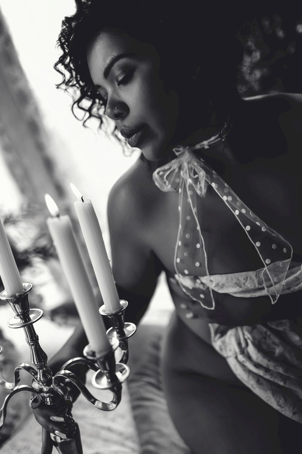 Black and white boudoir photo of a woman in lingerie gazing at candles in an elegant candelabra.