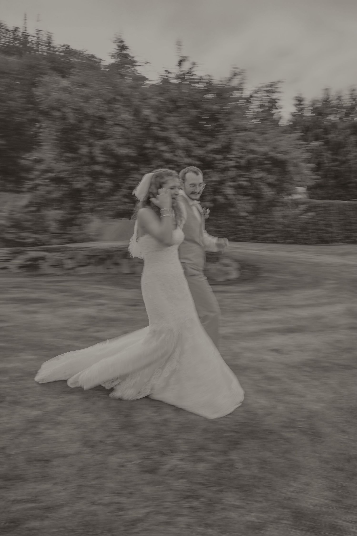 Black and white photo of a joyful bride and groom running together outdoors on their wedding day.