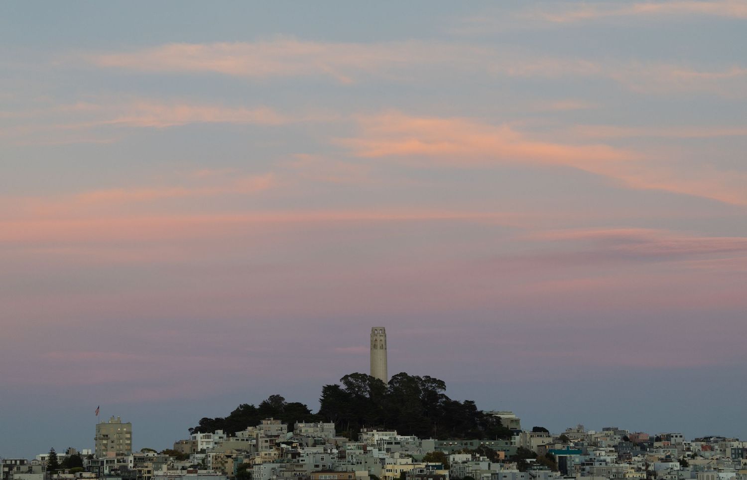 Coit Tower atop Telegraph Hill at sunset with pink clouds over San Francisco cityscape.