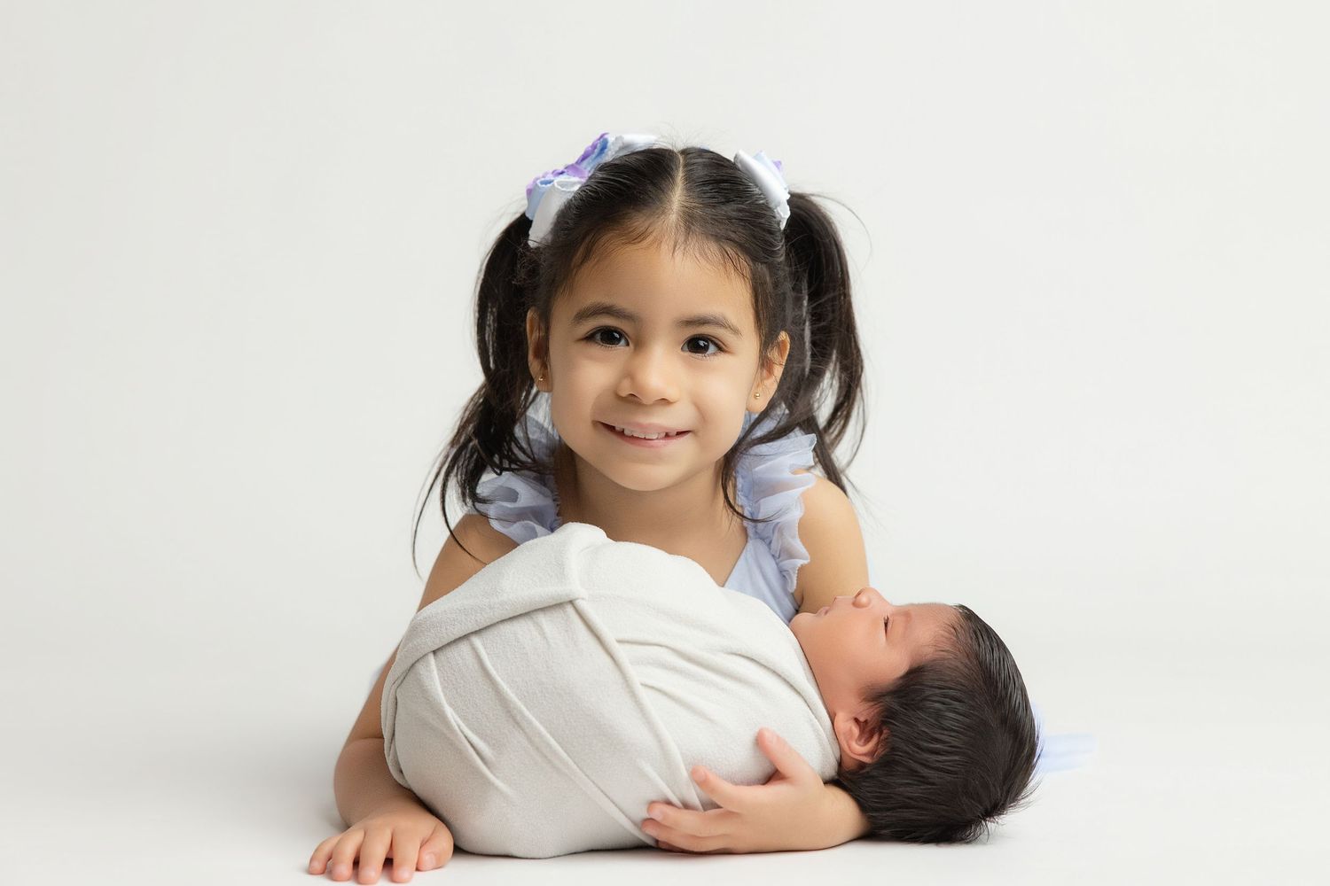 Newborn baby resting chin on hands inside a teal bucket with soft blanket, studio photography.
