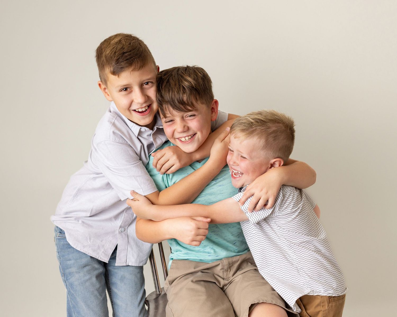 Three happy boys hugging and laughing together in a fun studio portrait photo.