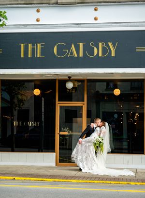 Bride and groom share a kiss outside The Gatsby venue, bride in lace gown holding bouquet.