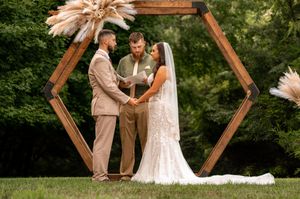 Bride and groom exchange vows outdoors under a hexagonal wooden arch adorned with pampas grass.