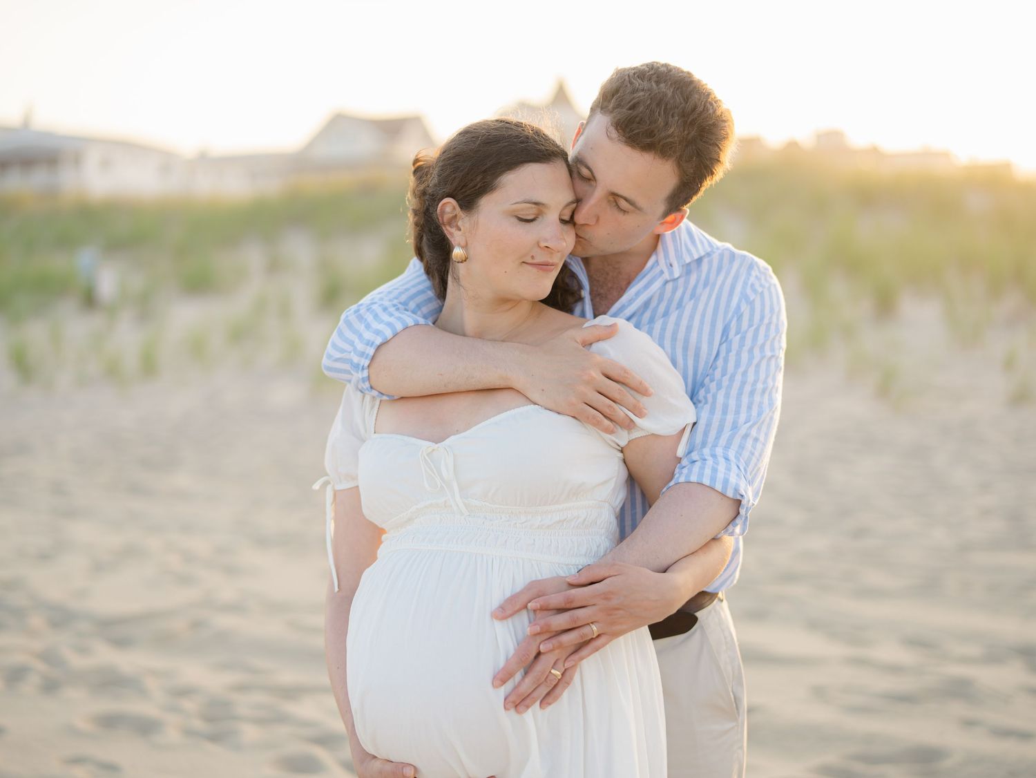 Husband embracing pregnant wife on Ocean Grove beach at sunset Monmouth County New Jersey.