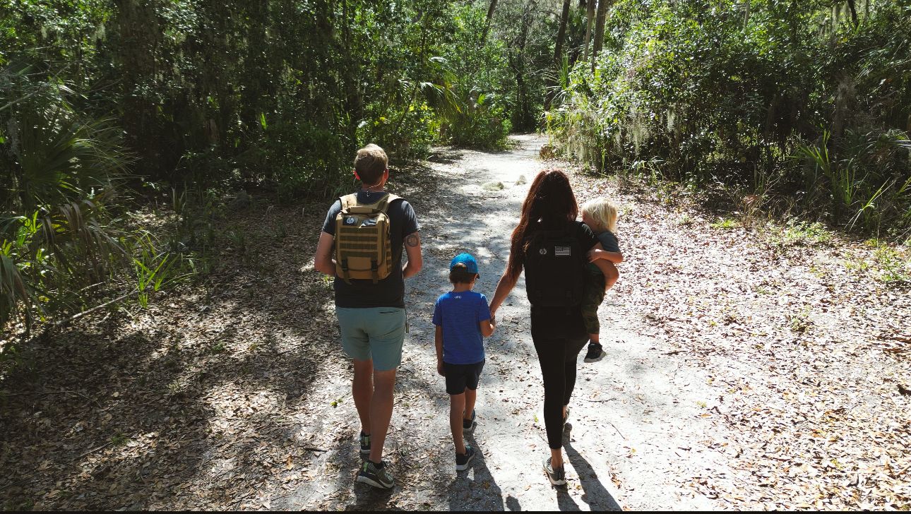 Family with two children hiking on a shaded forest trail surrounded by lush green trees.