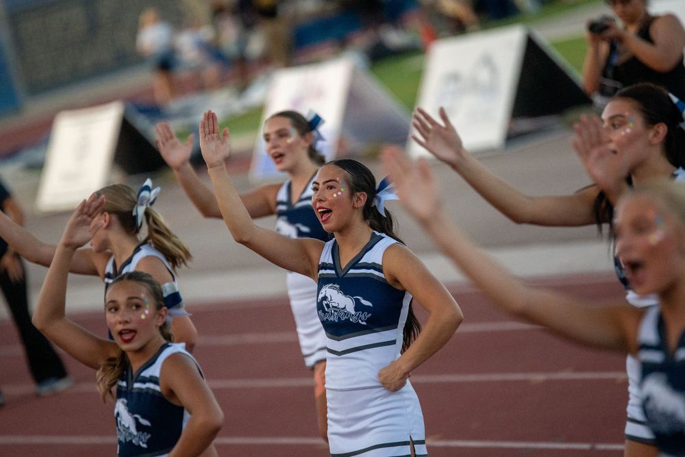 Cheerleaders in blue and white uniforms perform energetic routine on track field during outdoor sporting event.
