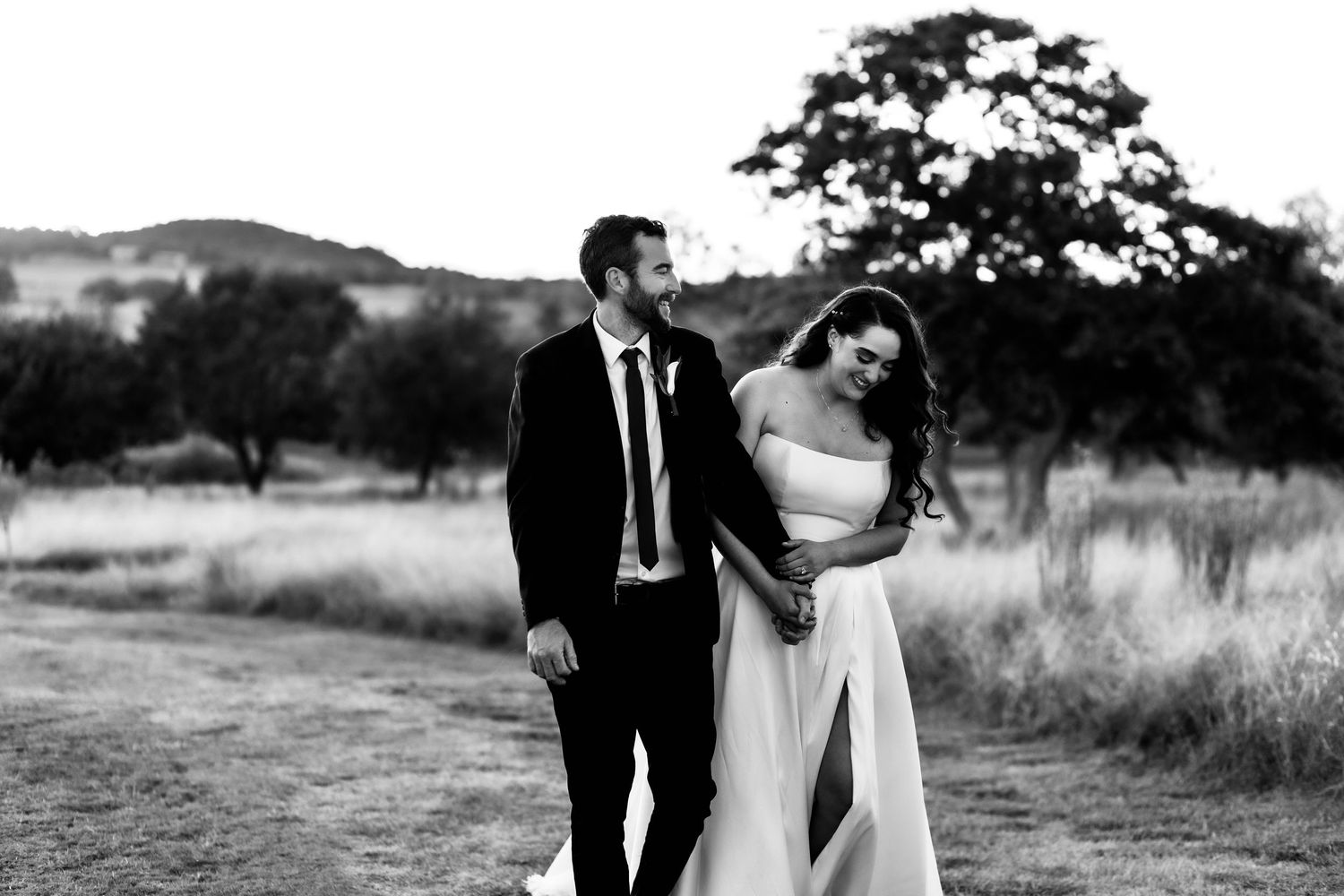 Black and white photo of bride and groom walking in field.