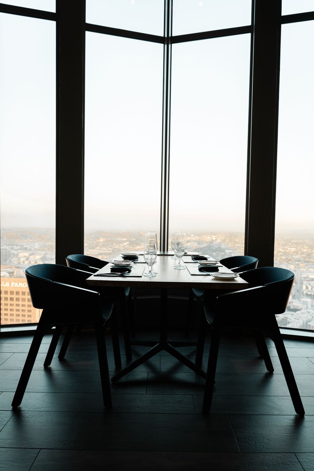 Elegant high-rise restaurant table set for four with panoramic city views through floor-to-ceiling windows.