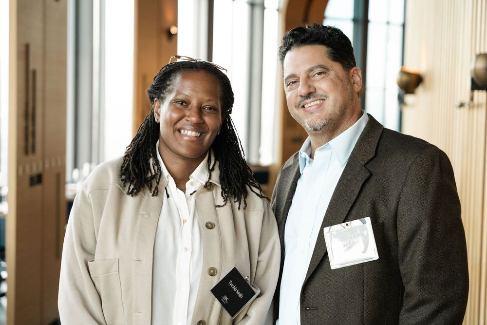 Two professionals smiling and posing together at a networking event in a modern venue.