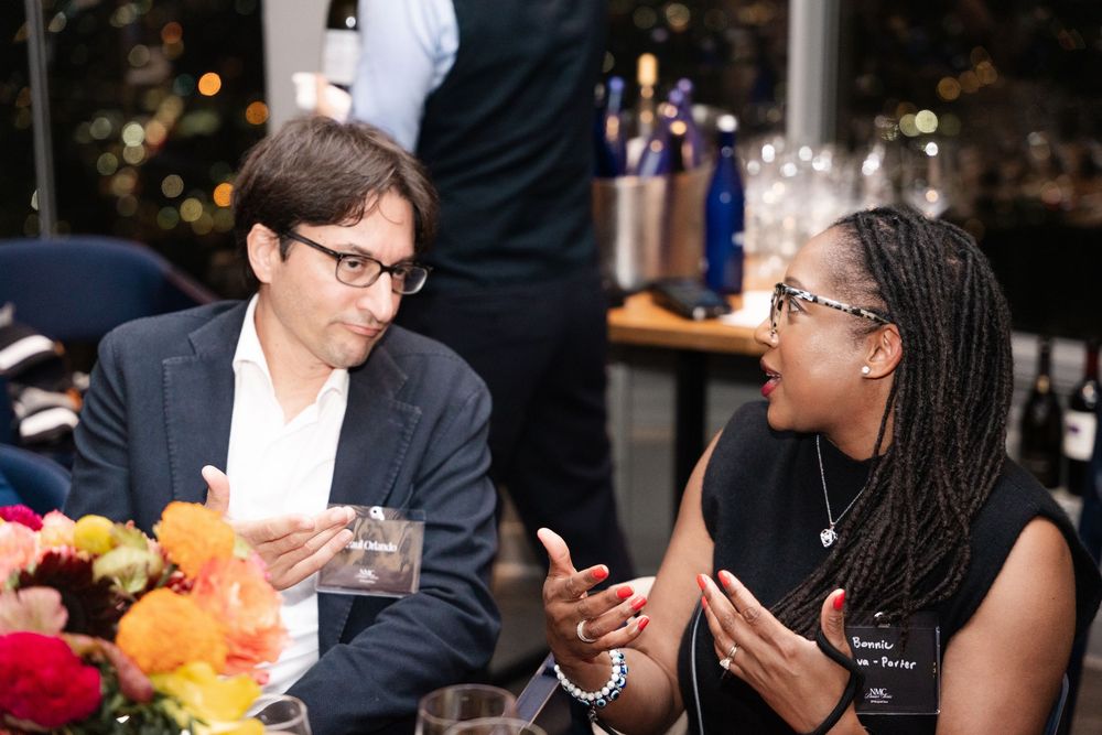 Two professionals engage in conversation at an elegant dinner event, with flowers and wine glasses on the table.