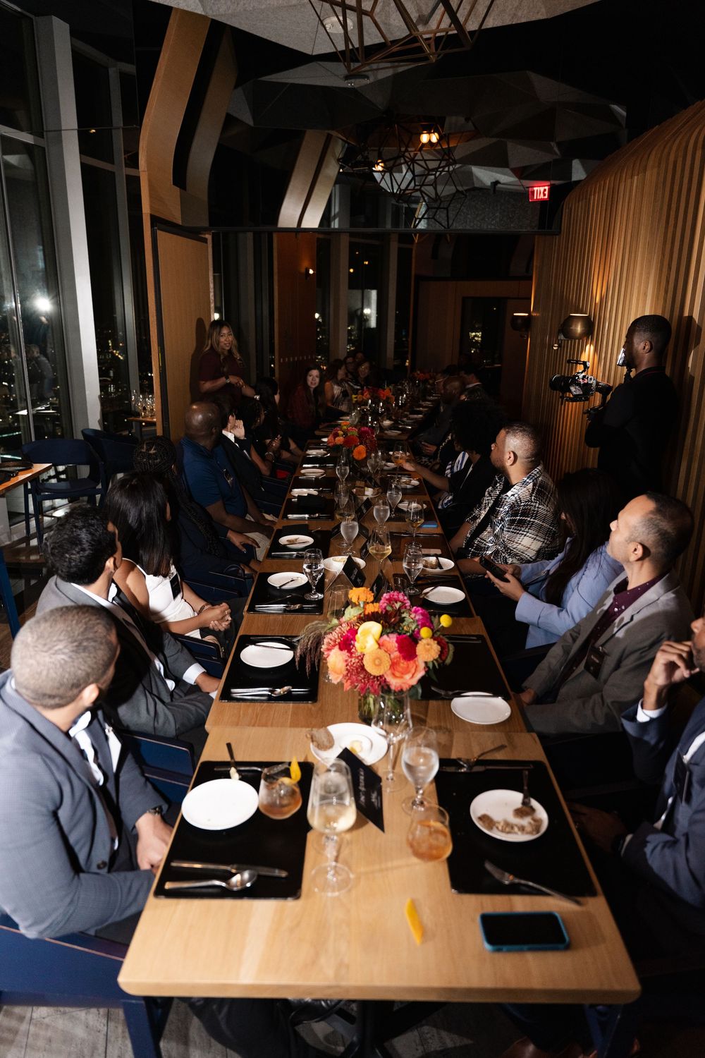 Elegant private dining event with guests seated at a long table adorned with floral centerpieces in an upscale restaurant.