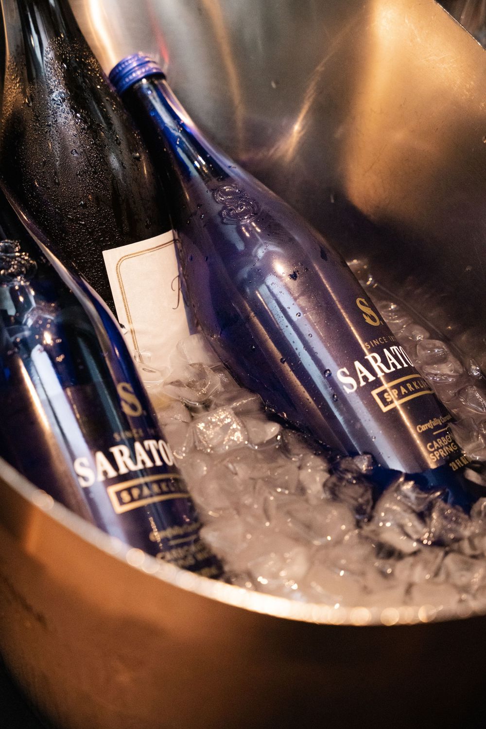 Blue Saratoga sparkling water bottles chilling in an ice-filled metallic bucket at an upscale event.