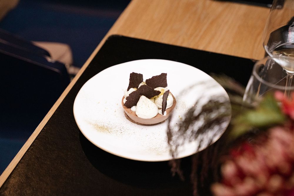 Elegant chocolate dessert with cream and dark chocolate shards on a white plate at a fine dining restaurant.