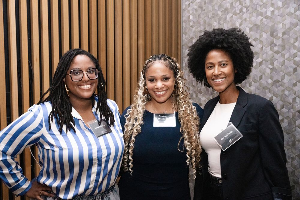Three women smiling and posing together at a professional networking event, wearing name badges.
