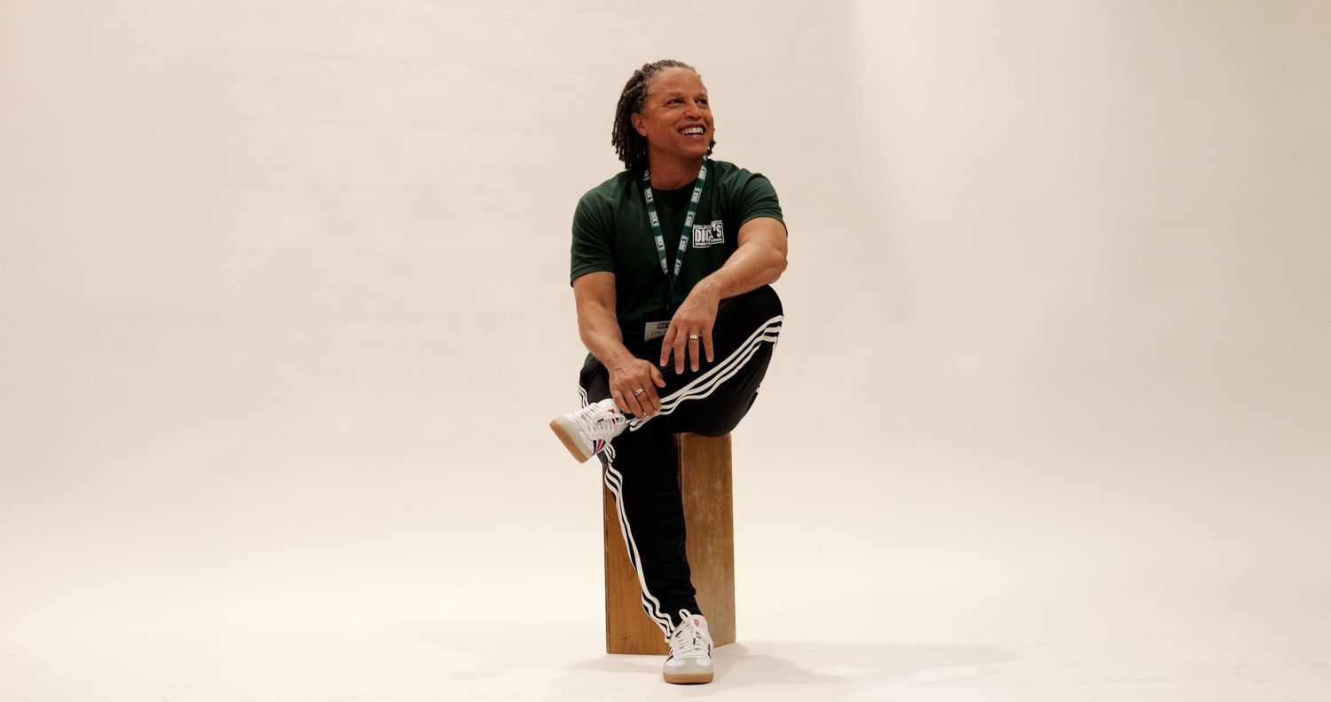 Person in black athletic wear sitting relaxed on a wooden block against a white background.