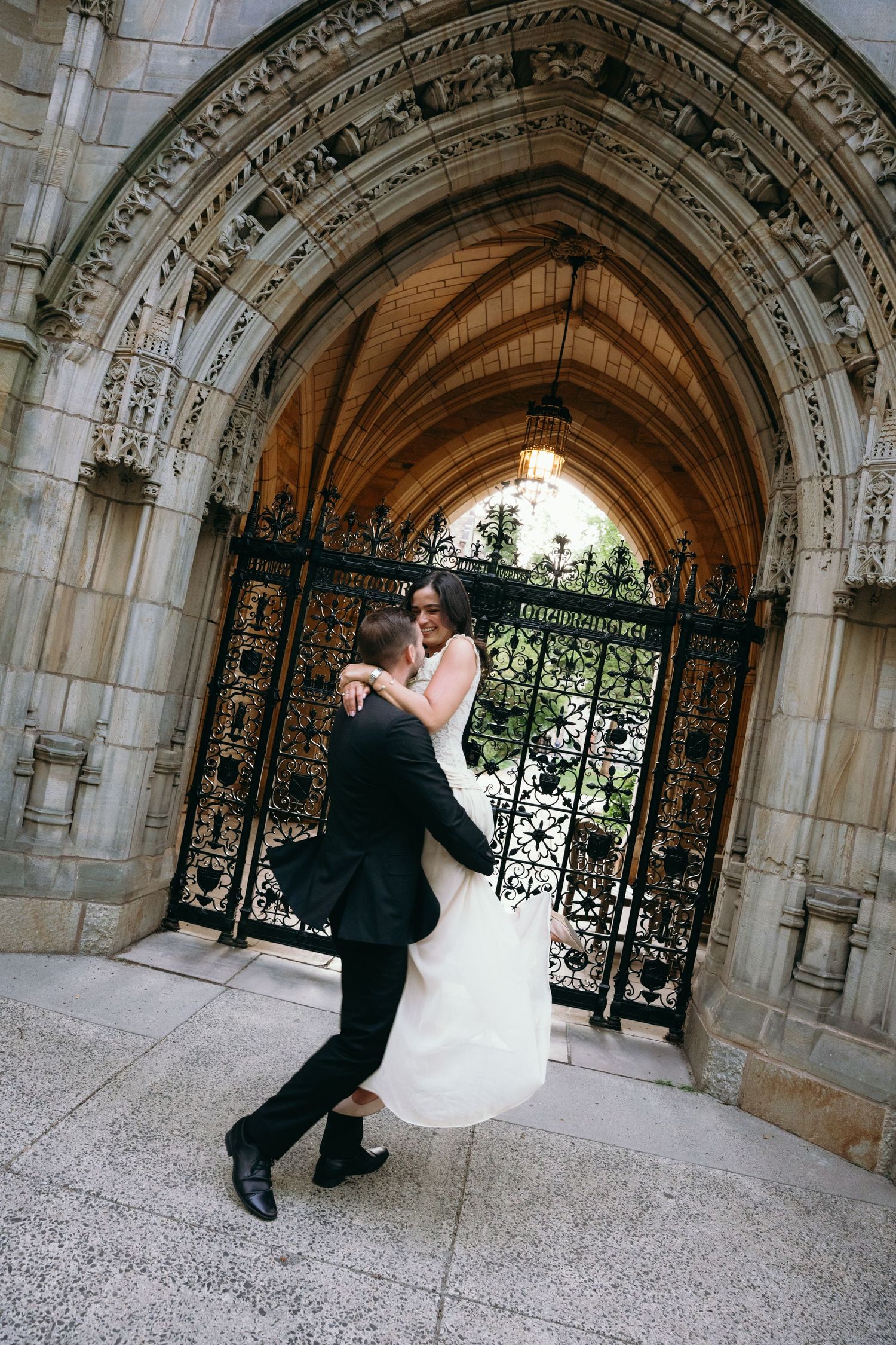 Bride and groom dancing under ornate Gothic stone archway with decorative iron gates at elegant wedding venue.