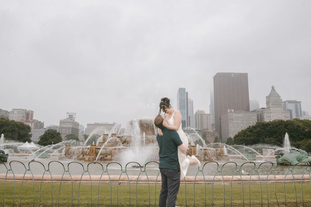 Couple embracing in front of Buckingham Fountain in Chicago with city skyline on a cloudy day.