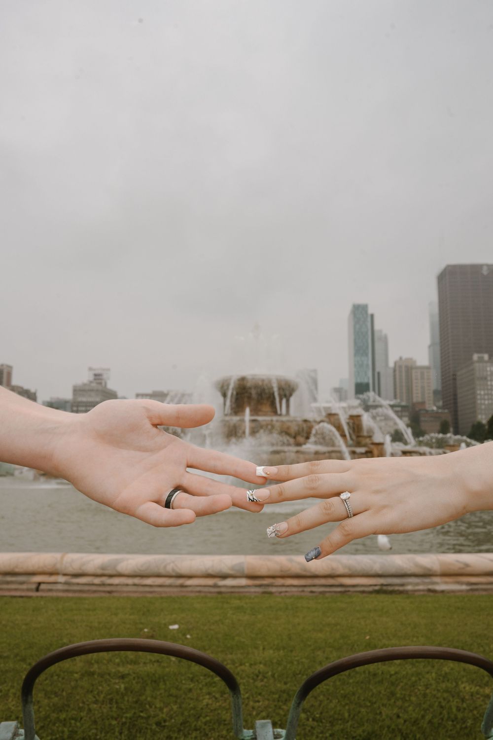 Two hands with rings reaching toward each other near Buckingham Fountain in Chicago on a cloudy day.
