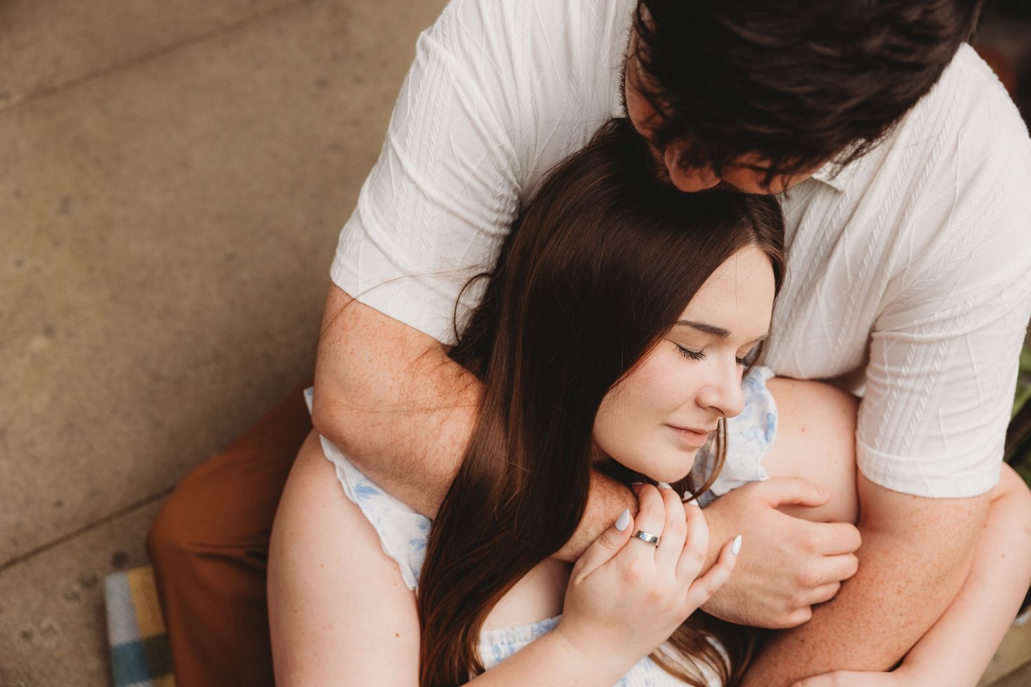 Couple sharing a tender embrace, woman with long brown hair resting against man in white shirt outdoors.
