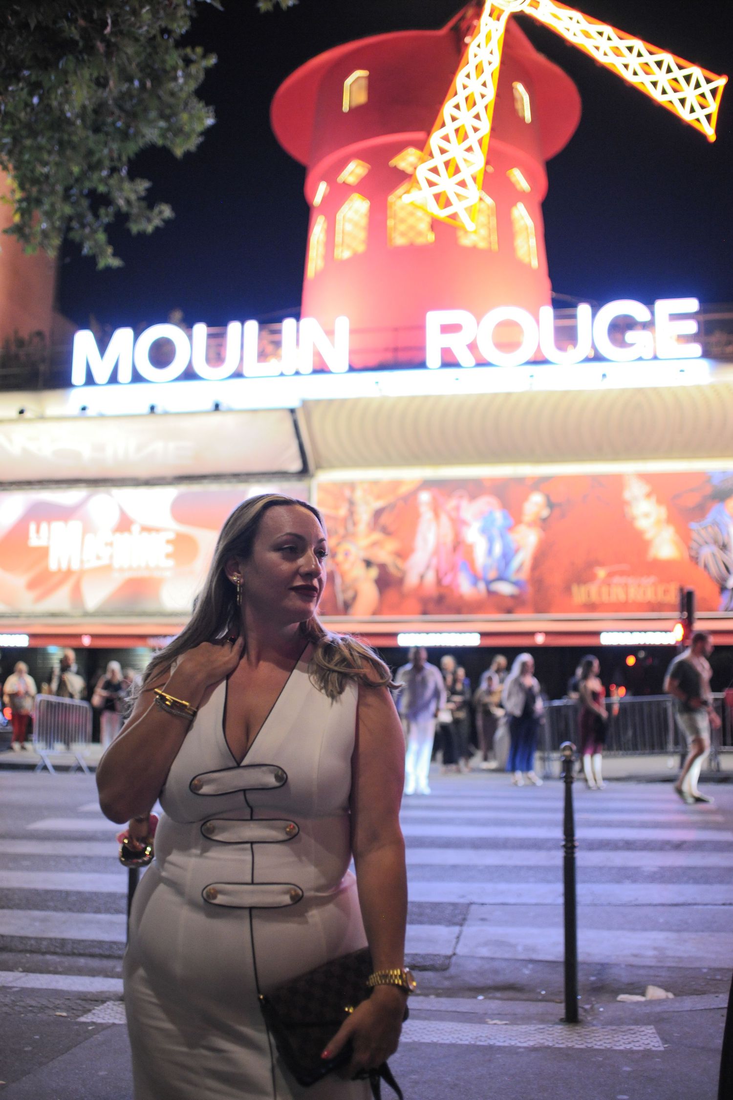 Woman in white dress posing at night in front of the iconic Moulin Rouge cabaret in Paris, France.