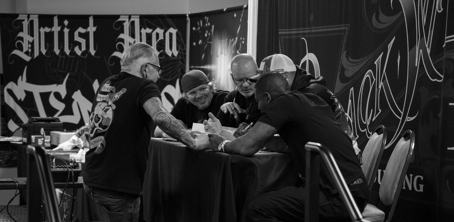 Black and white photo of tattoo artists working at an artist area booth at a tattoo convention.