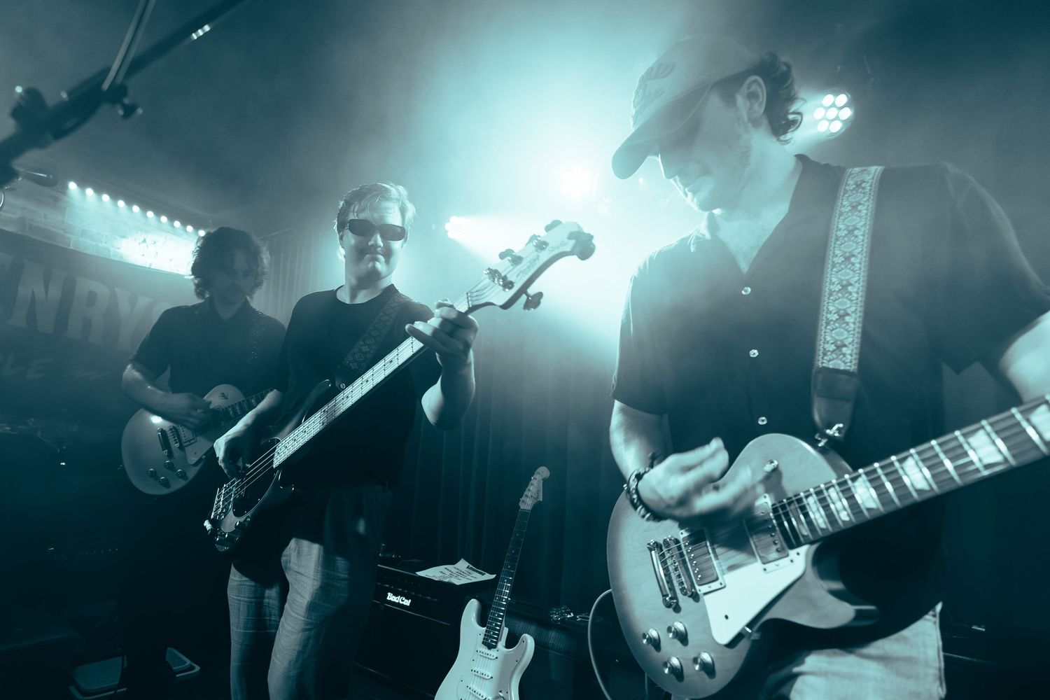Rock band performing on stage under dramatic blue-green lighting in a live music venue.