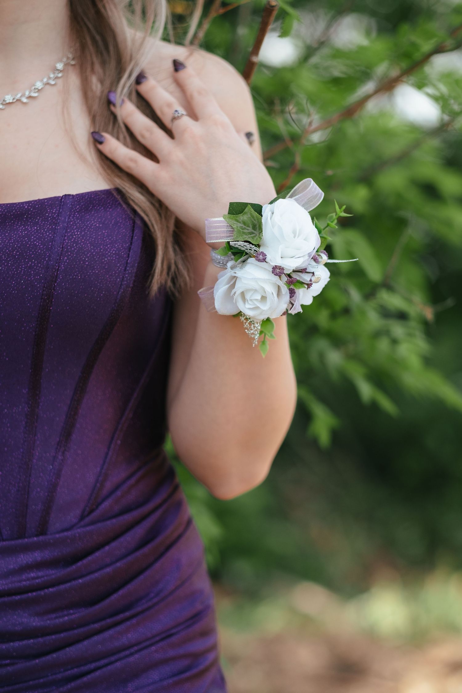 Smiling young woman in purple strapless dress leaning on wooden railing with lake and trees in background.