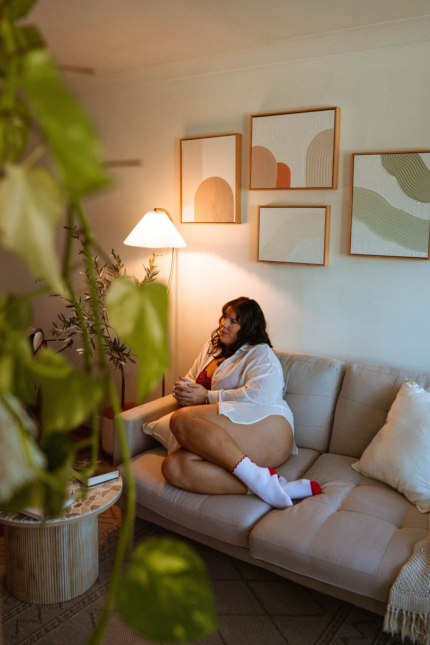 Woman relaxing on beige sofa in cozy living room with warm lamp light and abstract wall art.  Cairns boudoir photographer. Australia.
