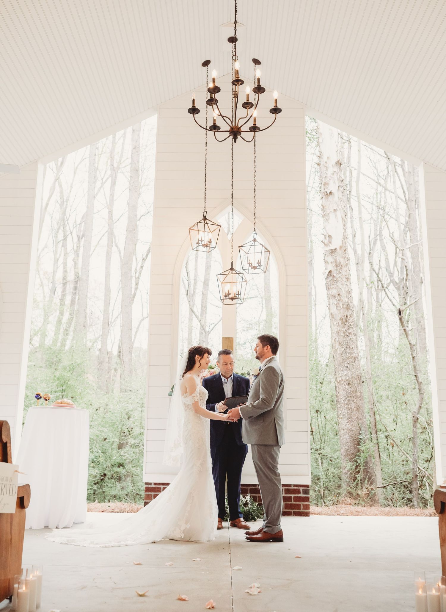 Bride and groom exchange rings during wedding ceremony with officiant, elegant venue with floral decor and large windows.