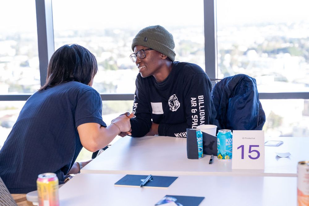 Two people shaking hands at a numbered table during a networking event with city views.