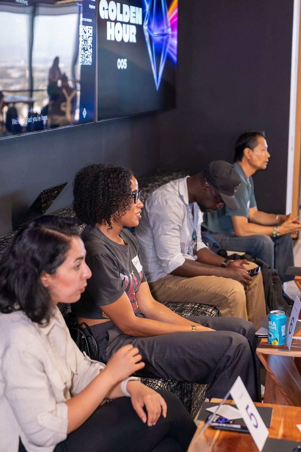 Group of diverse young adults seated in a row, focused on a screen displaying 'Golden Hour' at an indoor gaming event.
