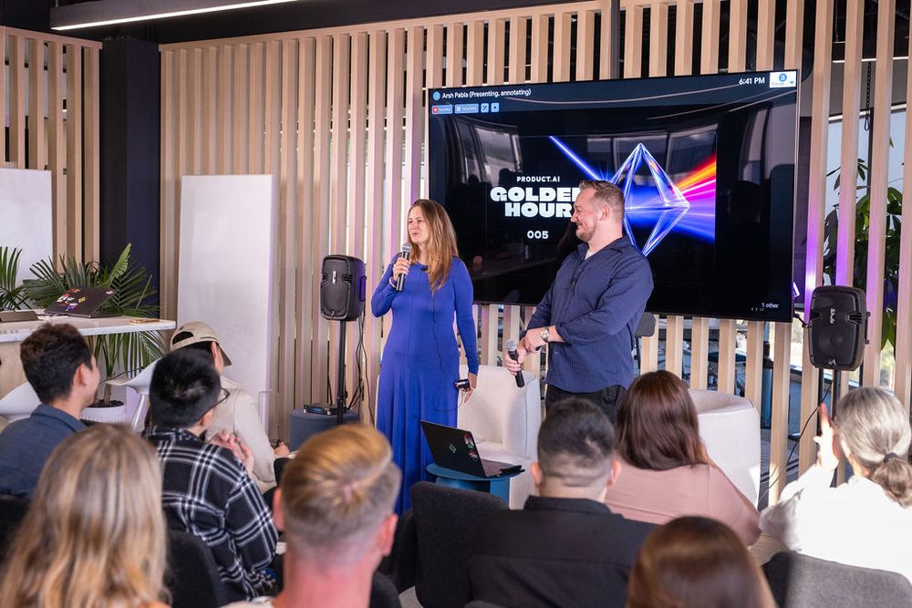 Woman in blue dress and man present Golden Hour event on stage to seated audience in modern venue.