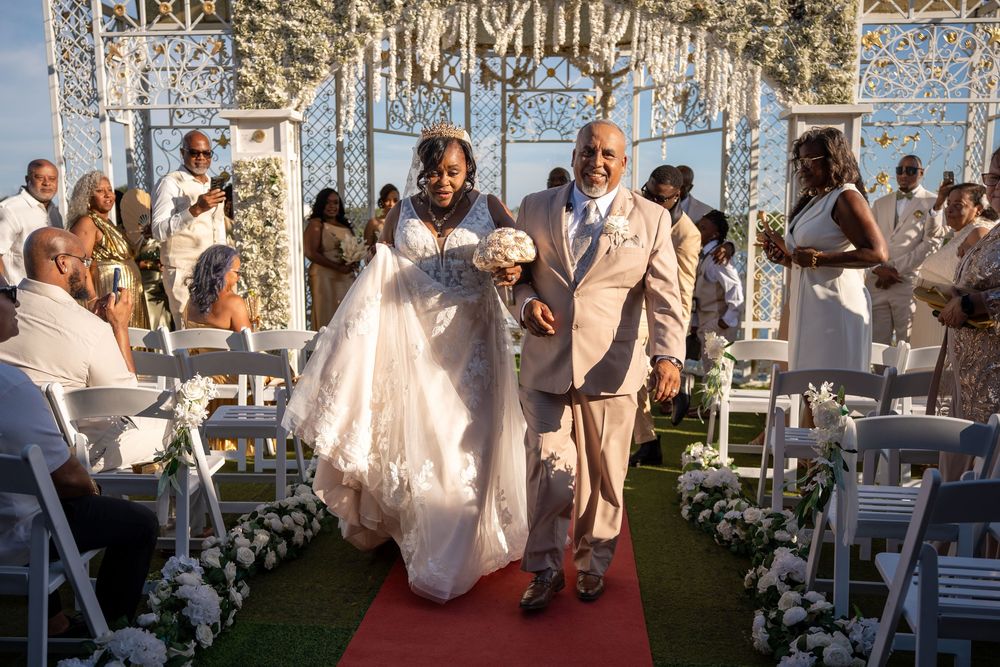 Bride and groom walk down the aisle at an elegant outdoor wedding ceremony with white floral arch.