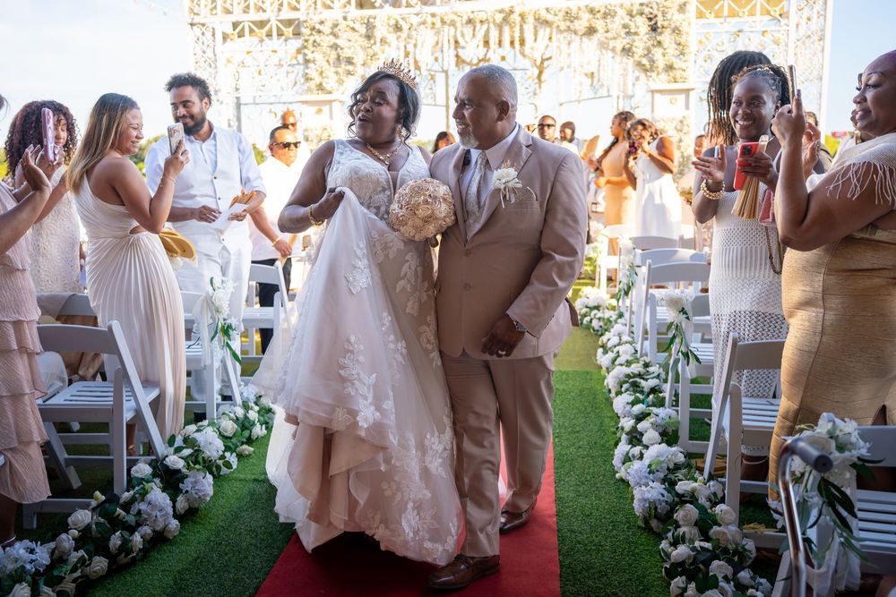 Joyful newlywed couple walks down the aisle at an elegant outdoor wedding ceremony with guests cheering.