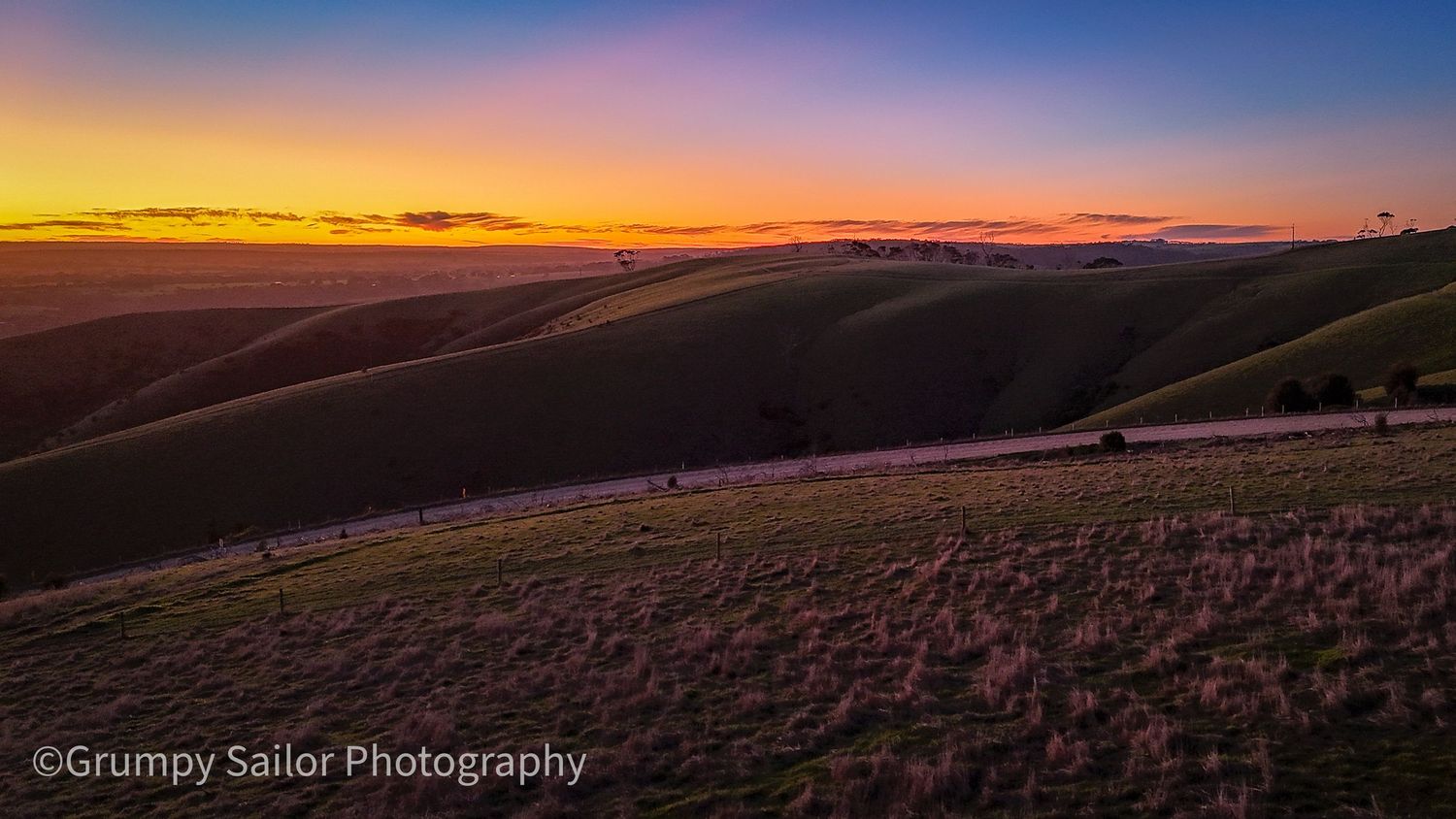 A stunning sunset over rolling green hills with vibrant orange and purple sky tones.