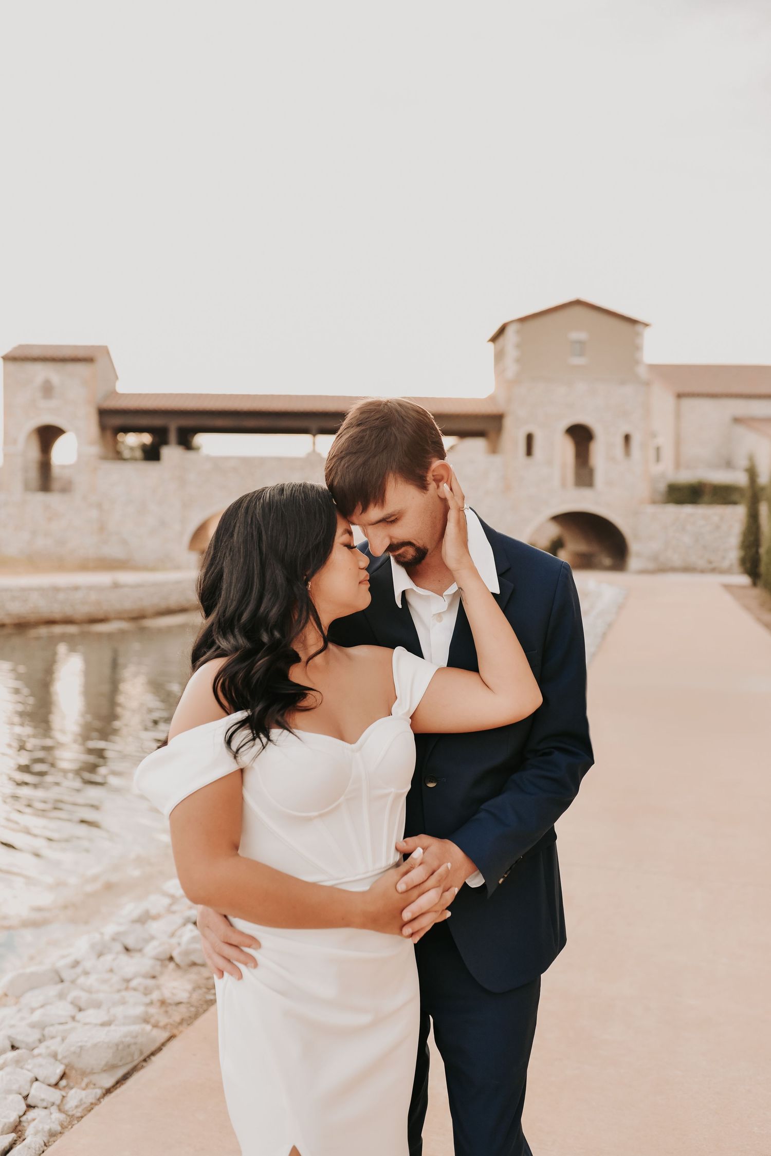 a bride and groom hand in hand along the waters edge at chapel at palacios
