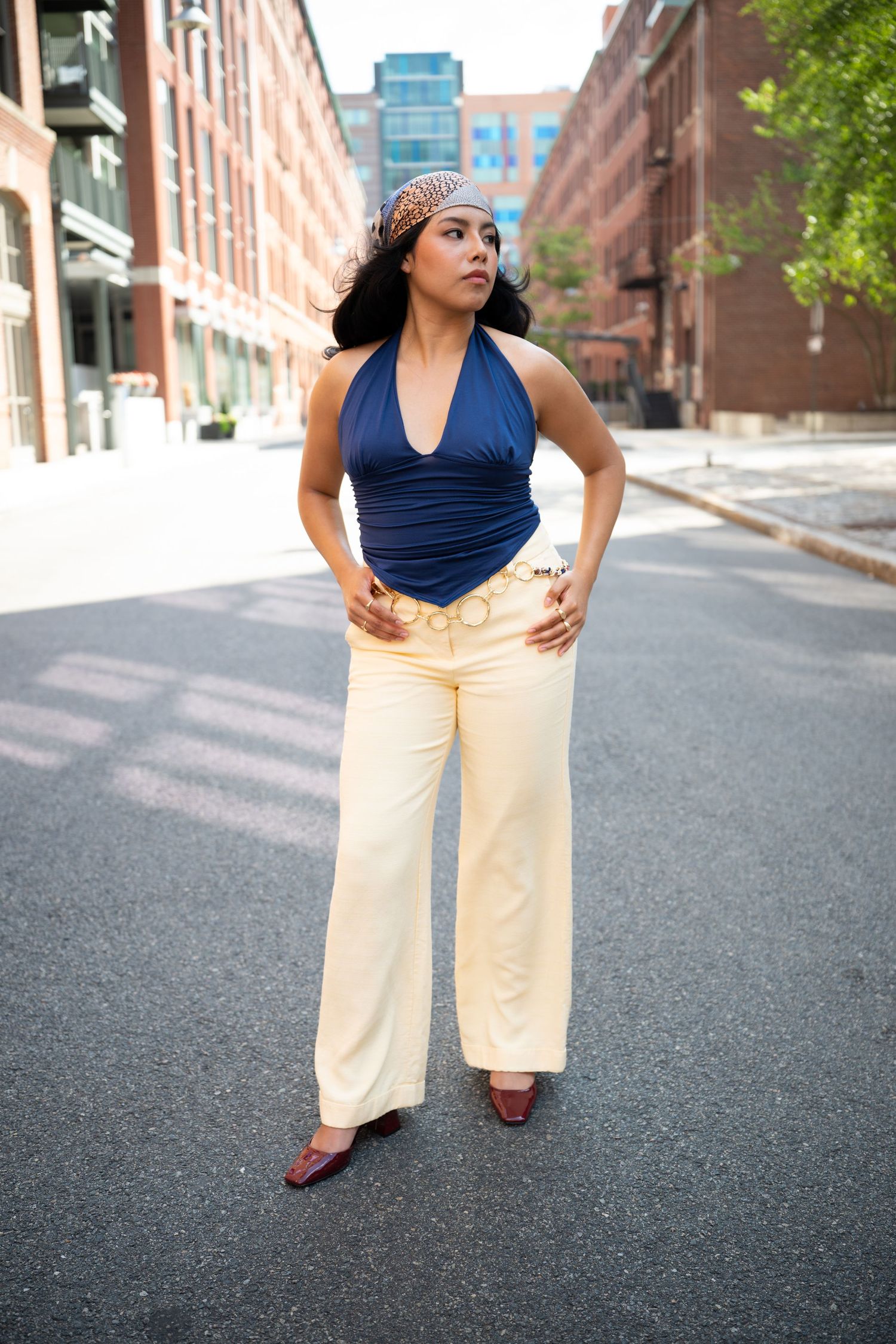 Woman in navy halter top and cream wide-leg pants poses confidently on urban street with brick buildings.