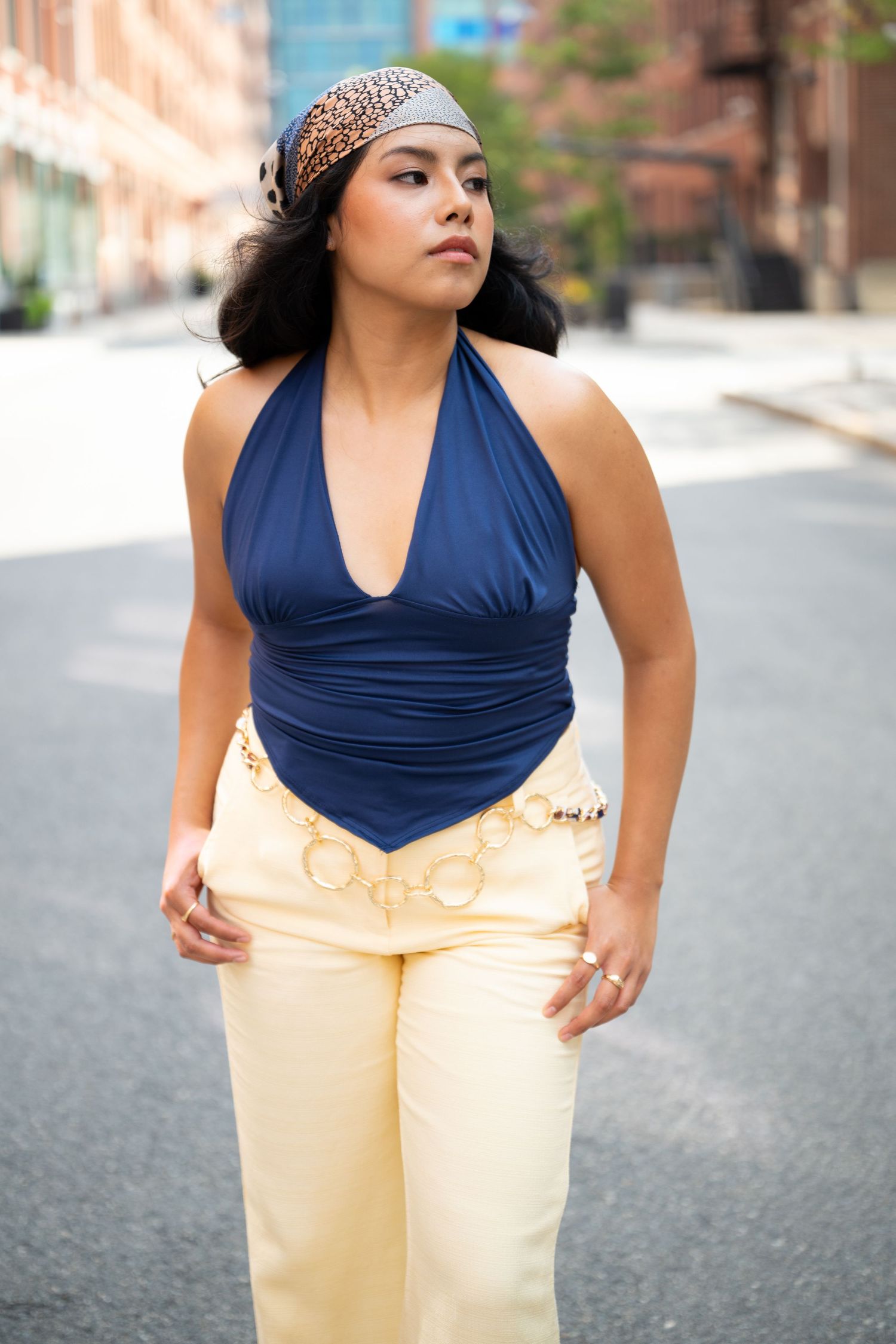Woman in navy halter top and cream pants with gold details poses on urban street wearing leopard headband.