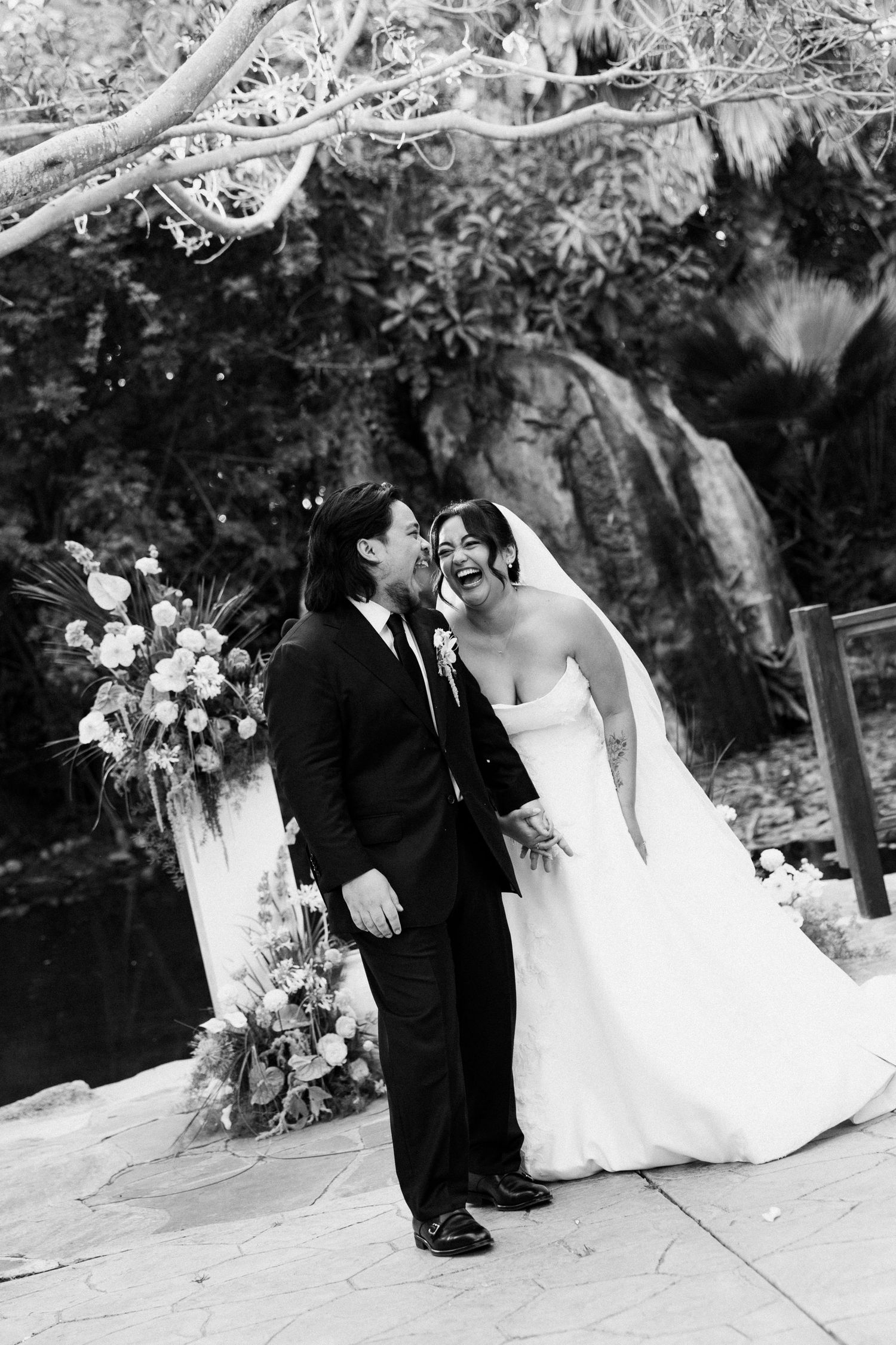 Black and white photo of a laughing bride and groom sharing a joyful moment at their outdoor wedding ceremony.