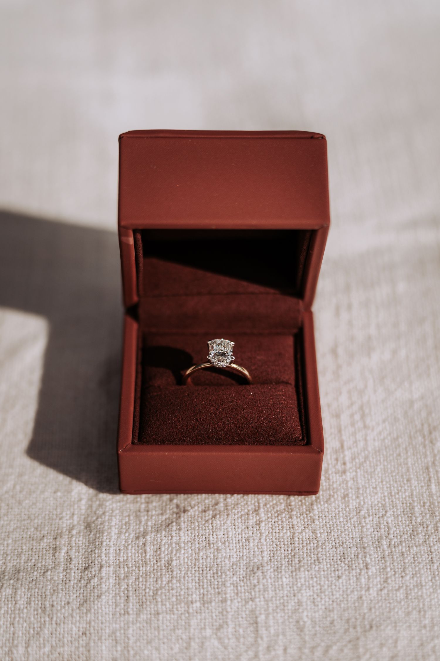 Elegant oval diamond solitaire engagement ring in open red velvet ring box.