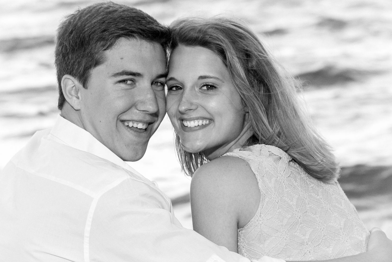 Black and white portrait of a smiling young couple embracing near the ocean.