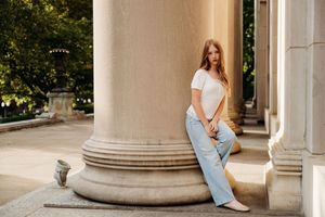Young woman in white tee and blue wide-leg jeans leaning against stone column outdoors.