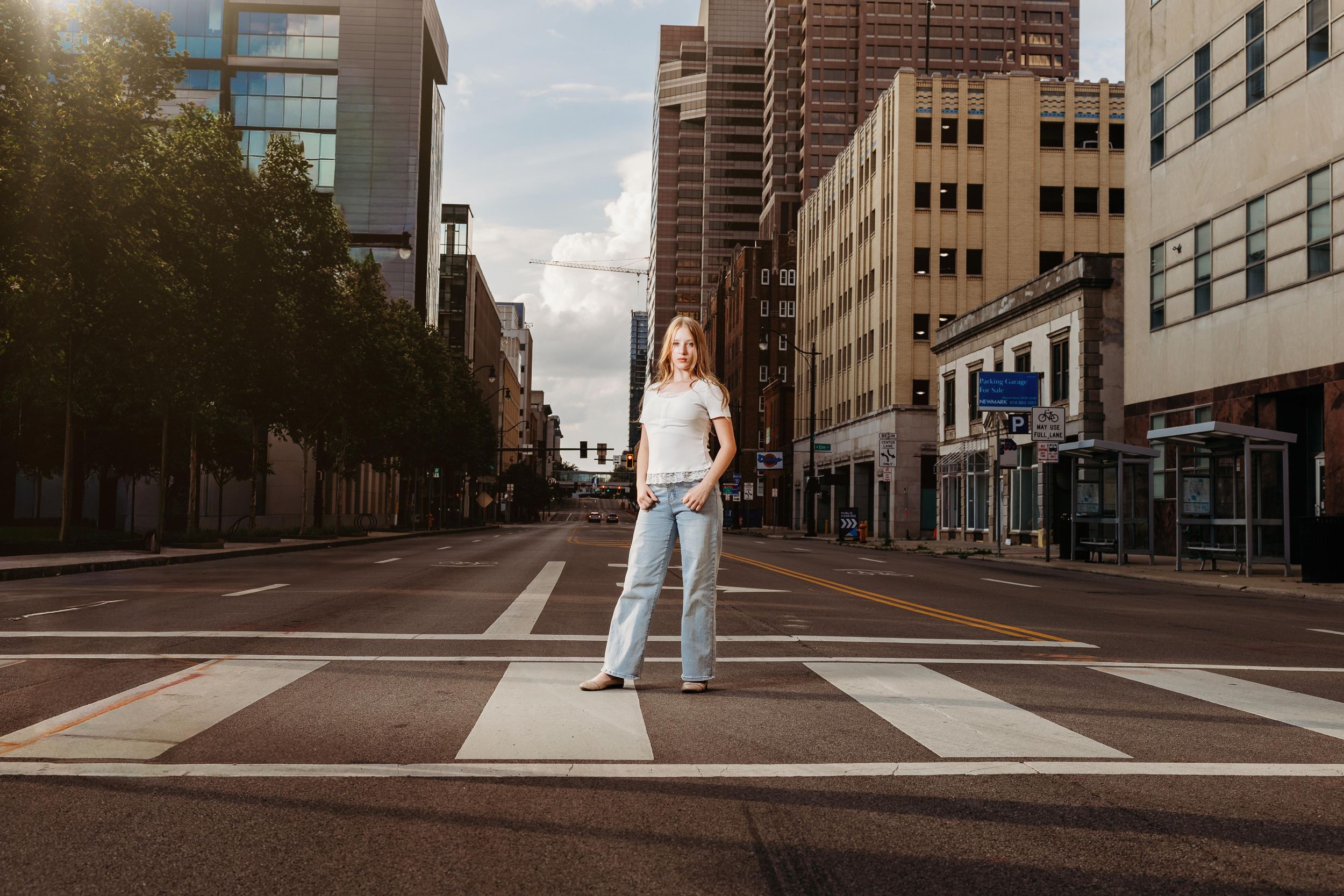 Young woman in white top and jeans stands confidently on a crosswalk in an empty urban downtown street.
