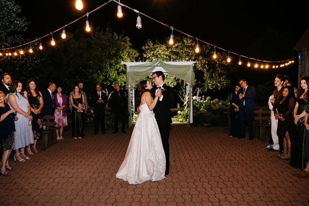Bride and groom share first dance under string lights at elegant outdoor wedding reception at night.