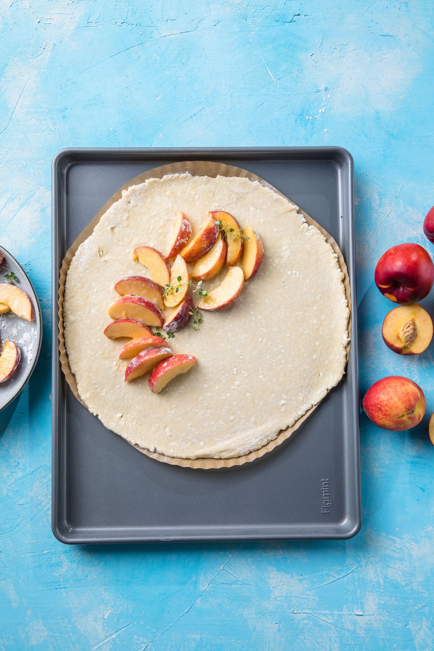 Unbaked peach galette on a baking tray with fresh sliced nectarines on a light blue background.