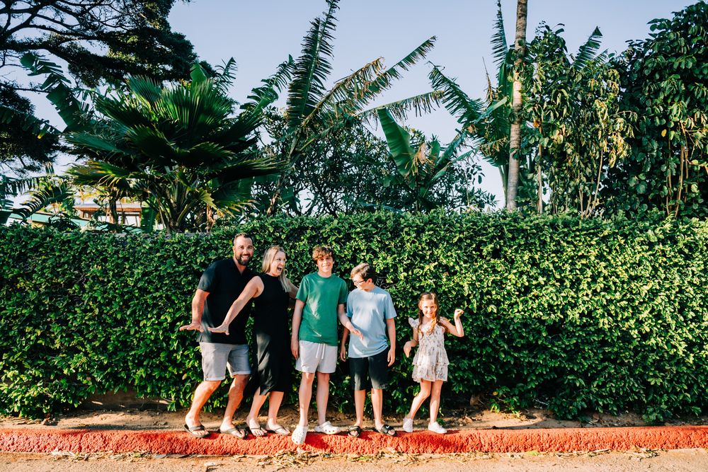 Family of five posing together in front of lush tropical greenery and palm trees on a sunny day.