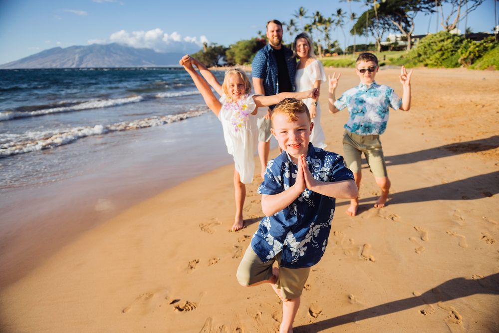 Family enjoying a sunny beach day in Maui with mountains in the background, children playing and posing for photos.