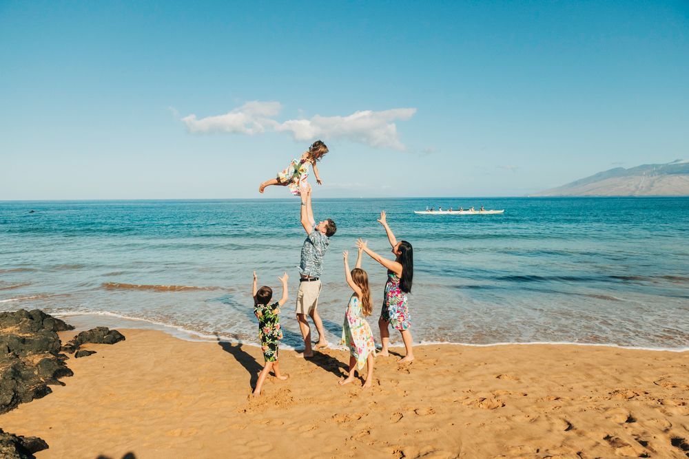 Family tossing child in the air joyfully on a sunny Hawaiian beach by the ocean.