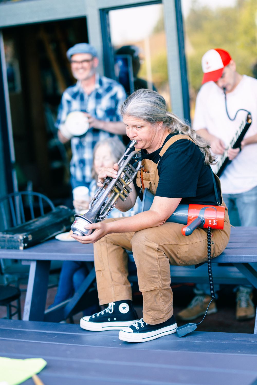 Musician plays trumpet seated on stage with band members performing behind her.