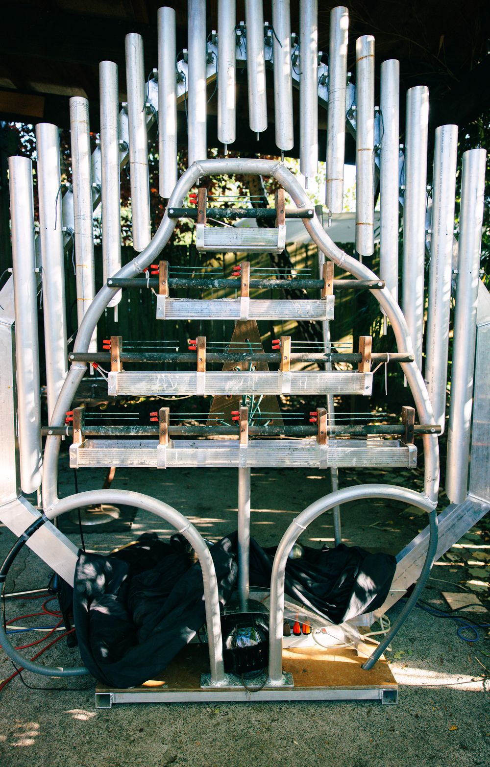 Metal pipe organ instrument frame with vertical silver tubes and red clamps displayed outdoors in sunlight.